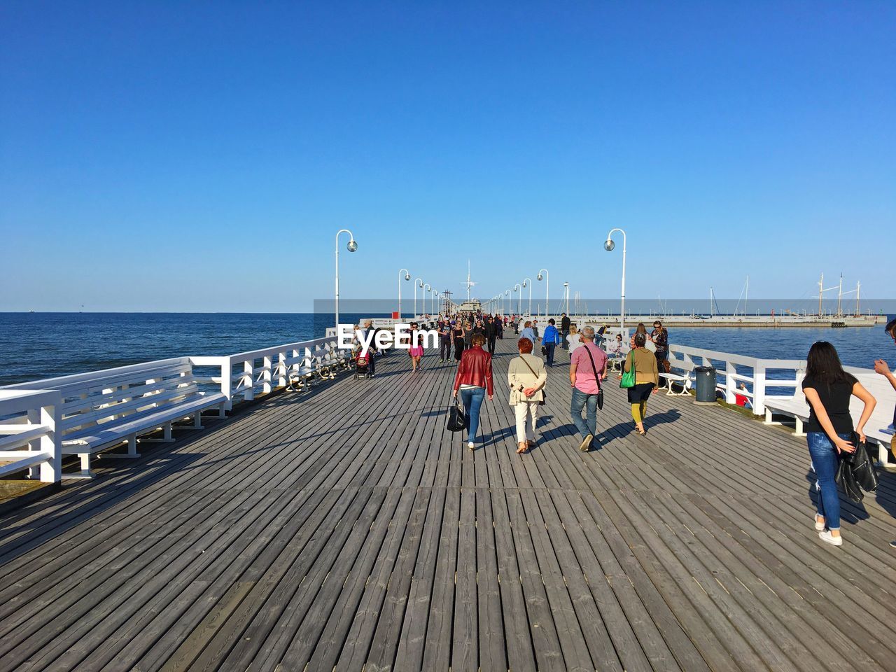 People walking on footbridge against clear blue sky
