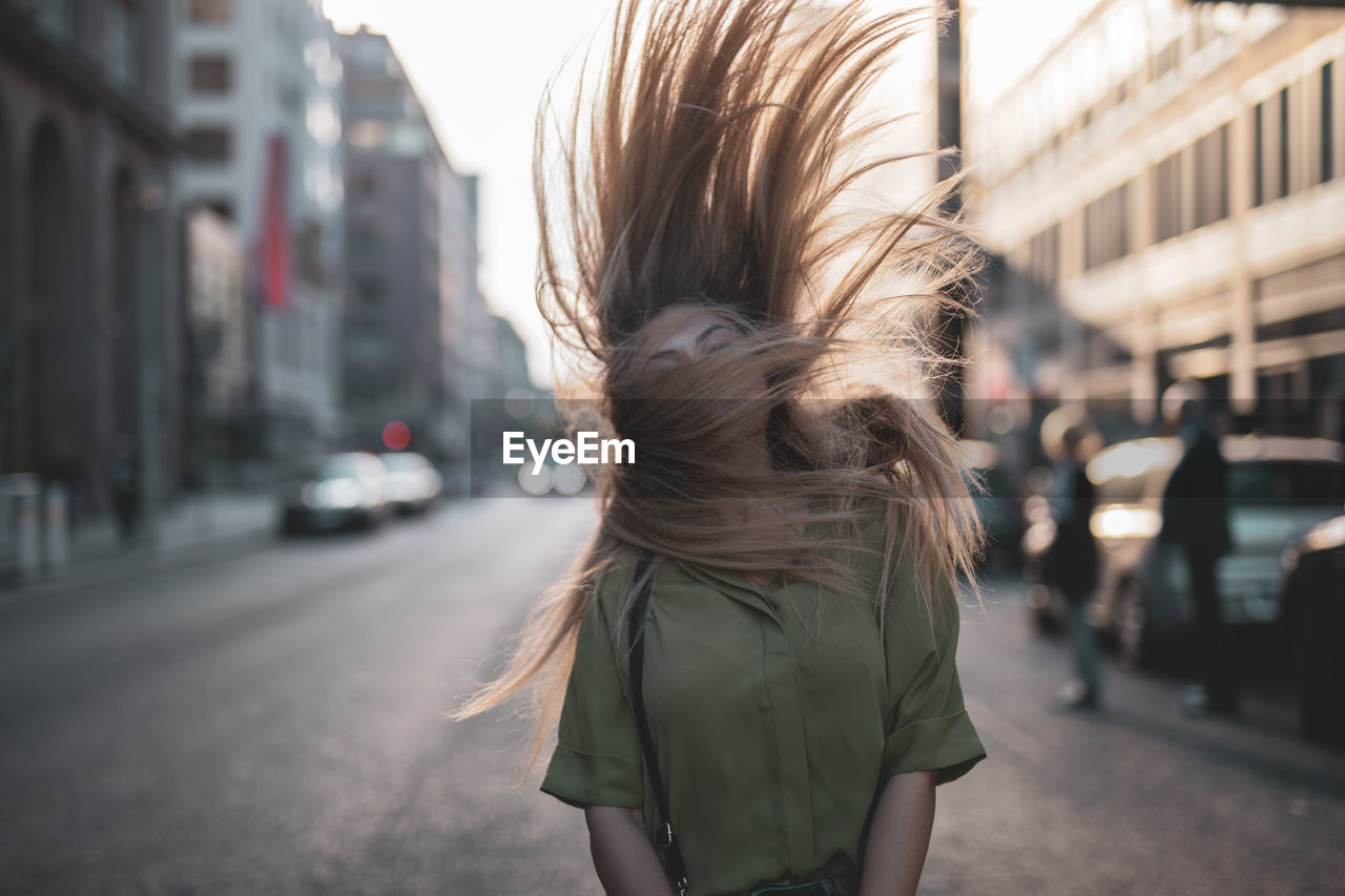 Young woman tossing hair while standing on city street