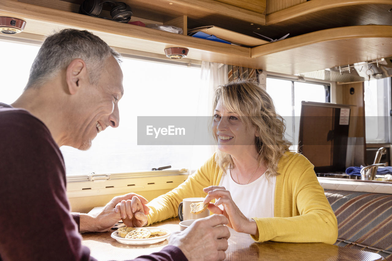 Happy mature couple having cookies at table in motor home