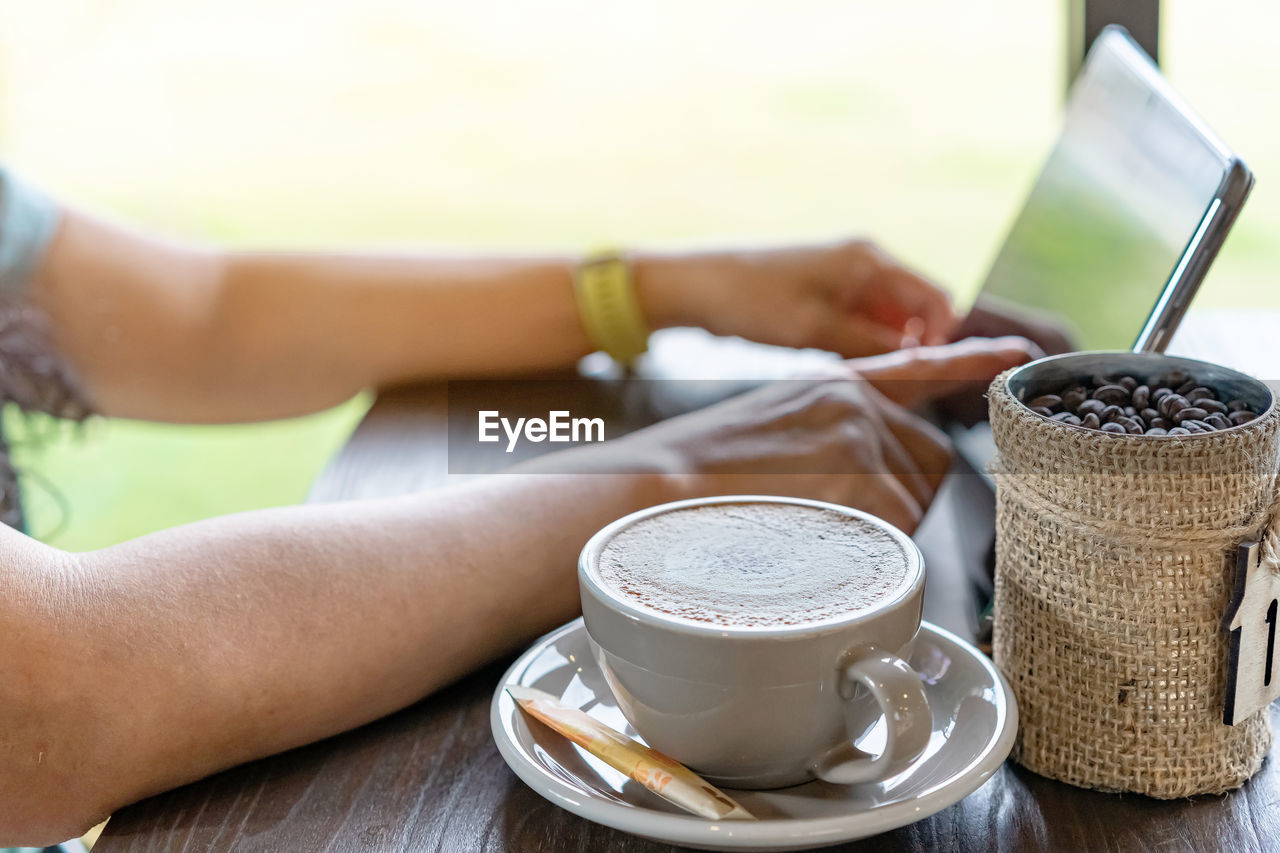 Hot cappuccino coffee for quarantined woman wear face mask and work from home by using tablet 