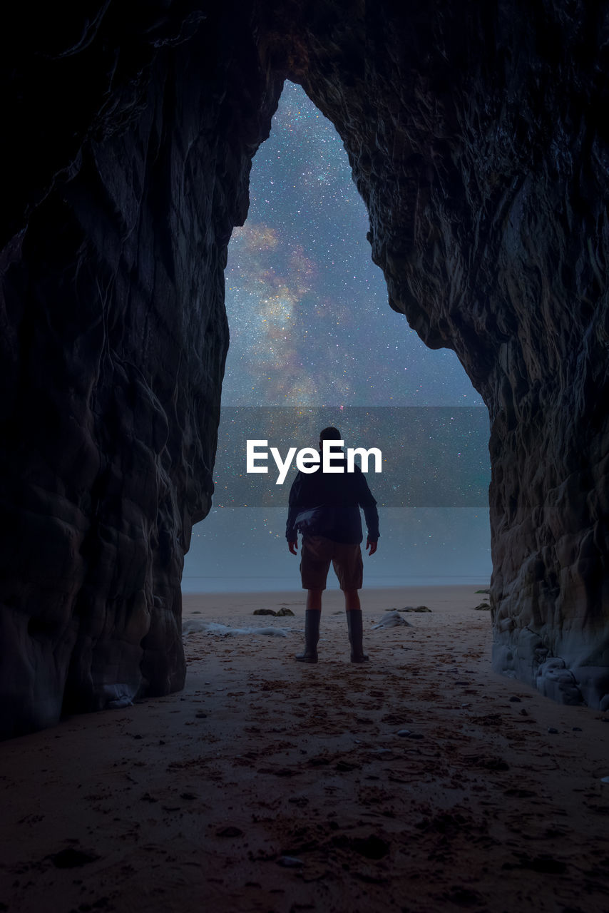 Rear view of man standing in sea cave looking at milky way