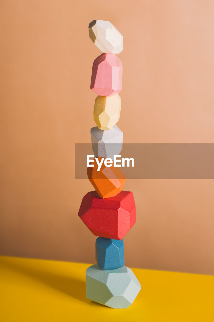 Wooden blocks in shapes of gems of various colors stacked on beige background in studio