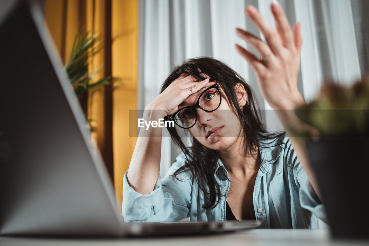 Low angle view of woman with head in hand working over laptop at home