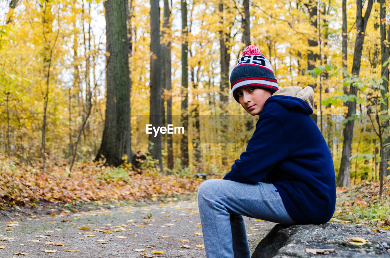 Portrait of smiling boy sitting in forest during autumn