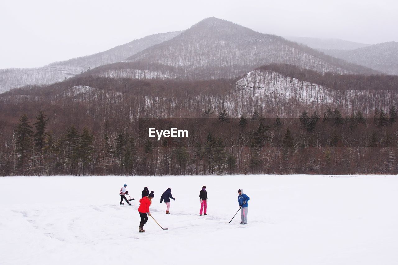 People playing ice hockey against snowcapped mountain