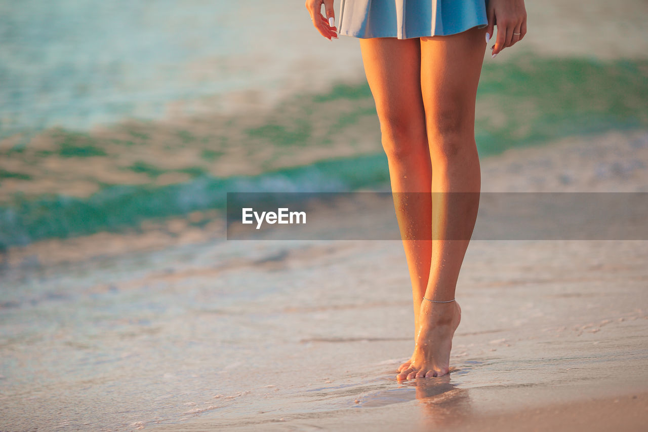 low section of woman standing on sand at beach