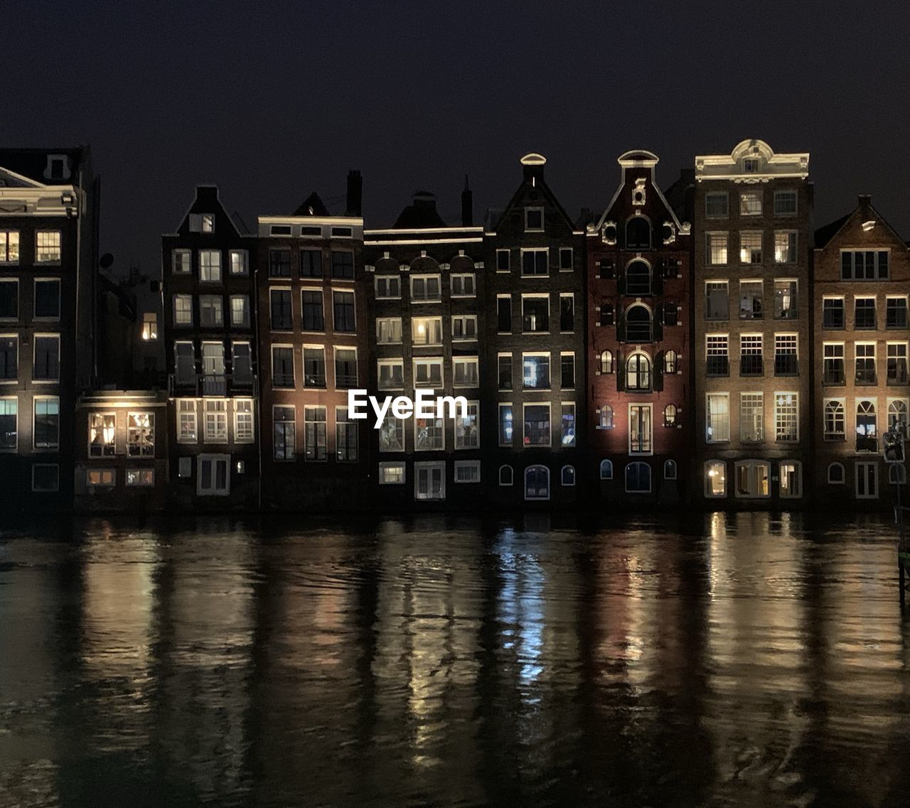 Illuminated buildings by river against sky at night