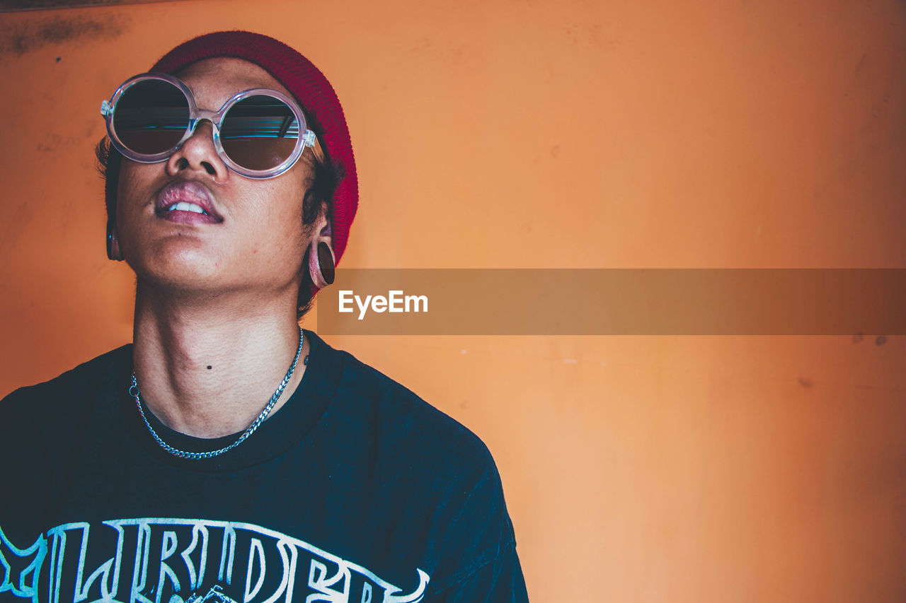 Young man wearing sunglasses standing against wall