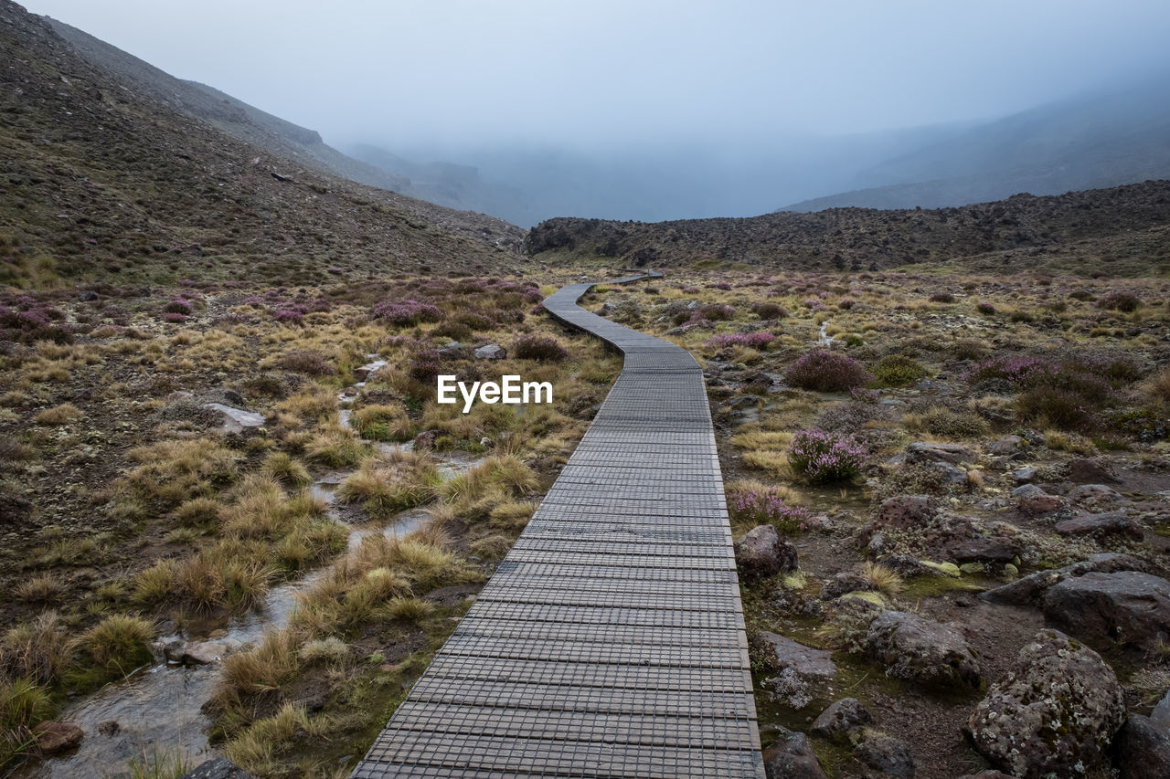 Narrow footpath leading towards mountain against sky