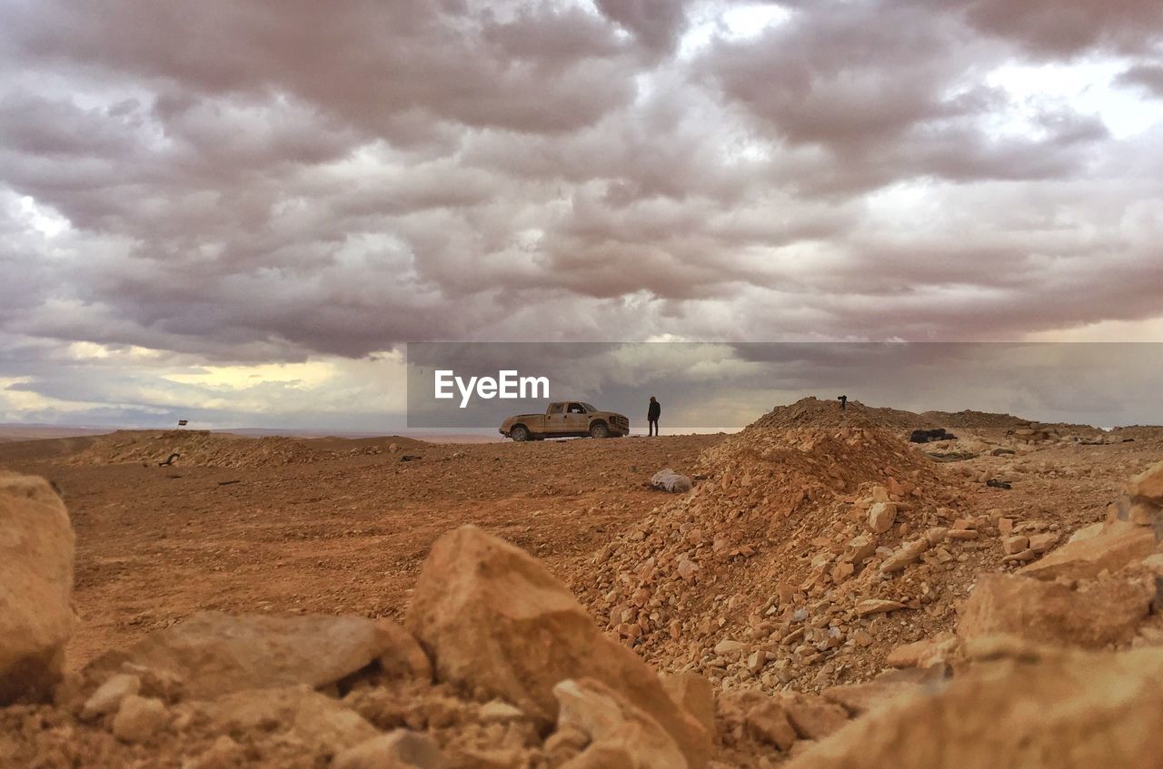 Person with car standing on land against cloudy sky