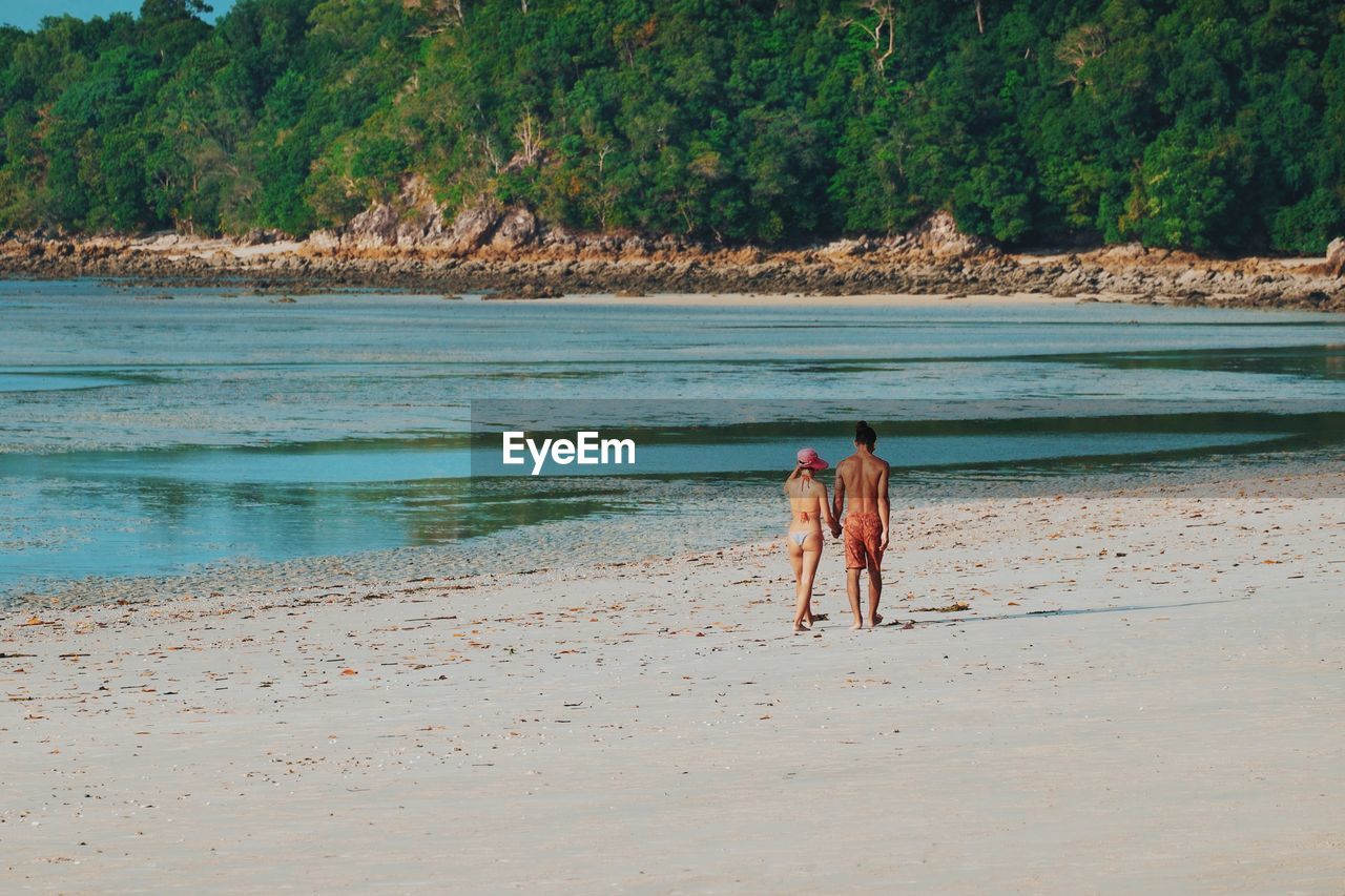 PEOPLE STANDING ON BEACH BY SEA AGAINST TREES