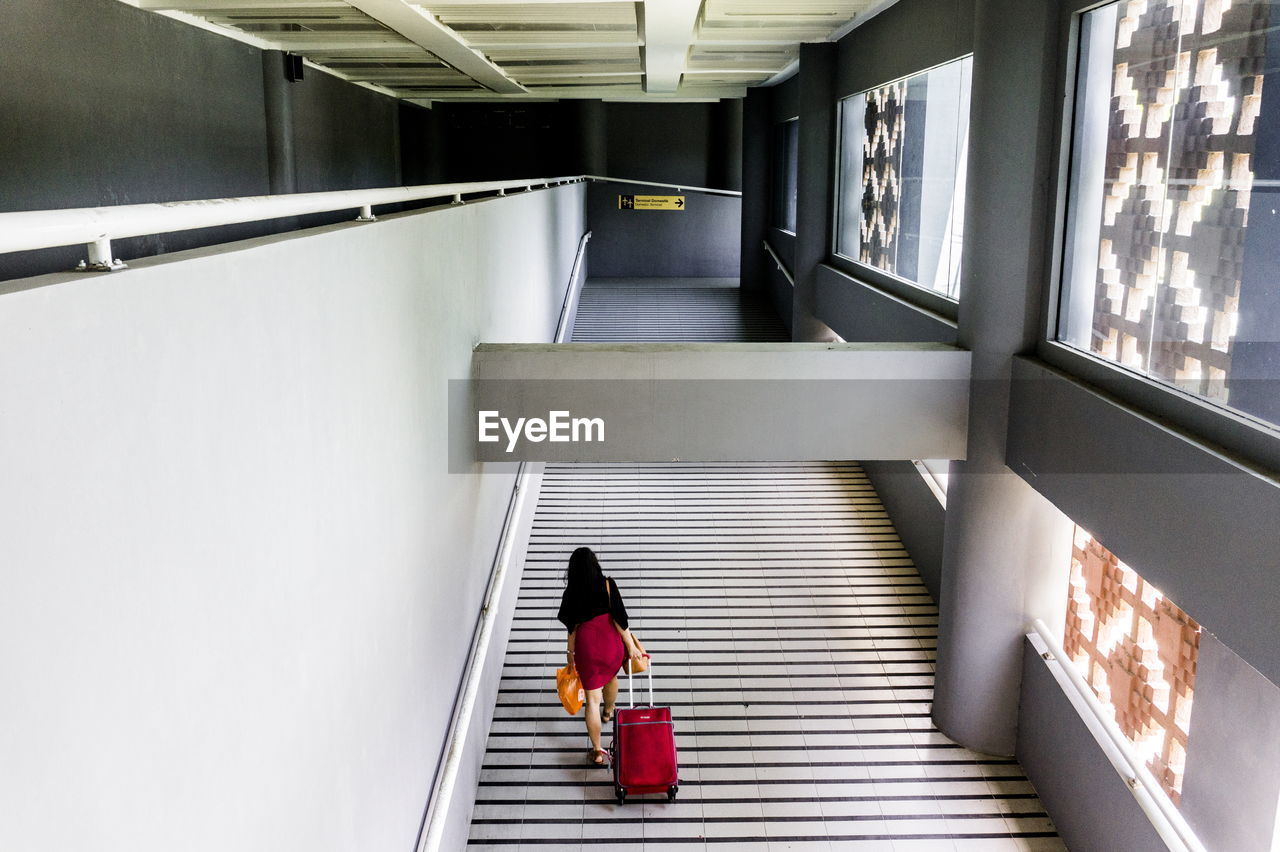 REAR VIEW OF WOMAN STANDING BY ESCALATOR