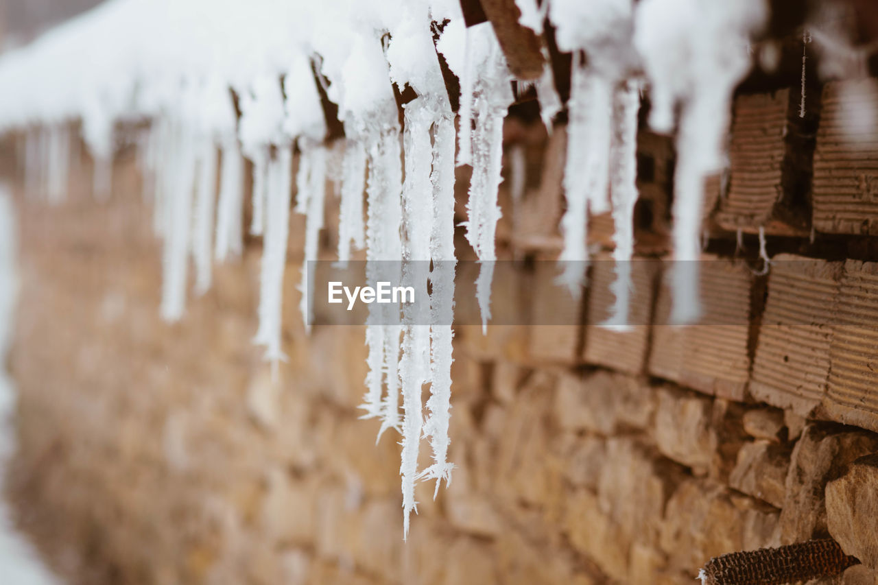 CLOSE-UP OF ICICLES HANGING FROM WOOD
