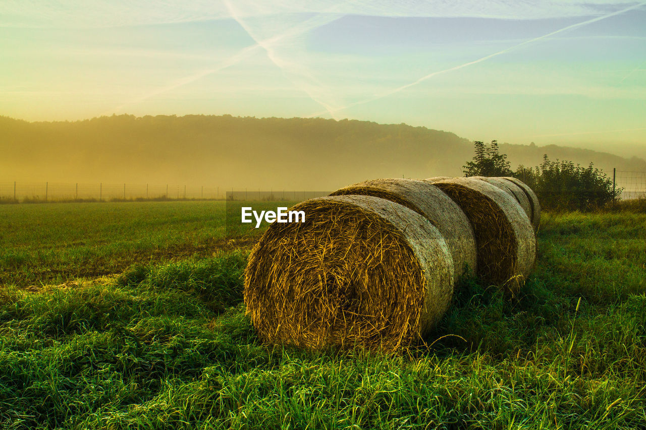 Hay bales on field against sky during sunset