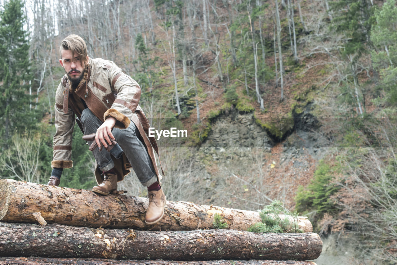 Portrait of young man sitting on logs in forest