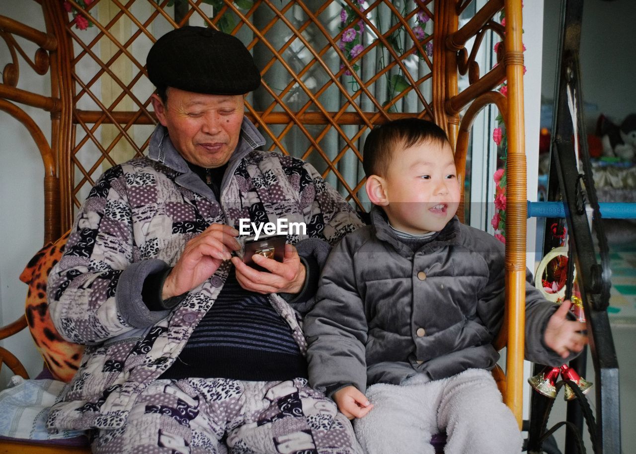 FULL LENGTH OF BOY SITTING IN A MAN HOLDING A BABY