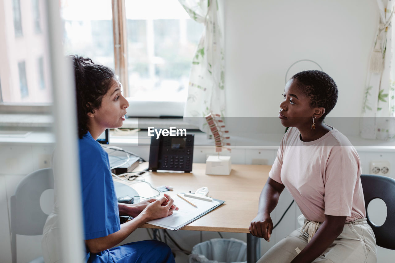 Female healthcare worker explaining medical records to young patient in office