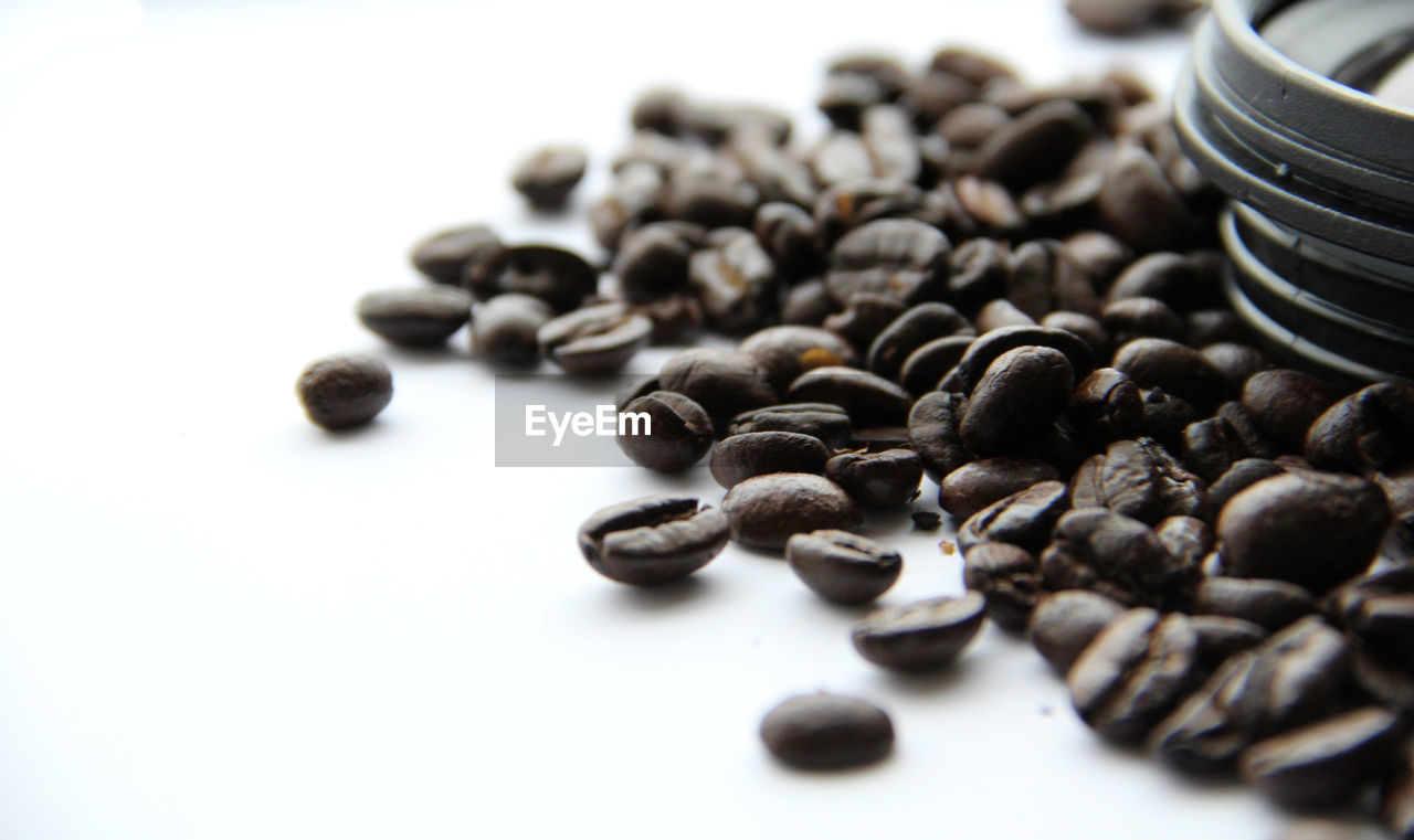 Close-up of lens on roasted coffee beans against white background