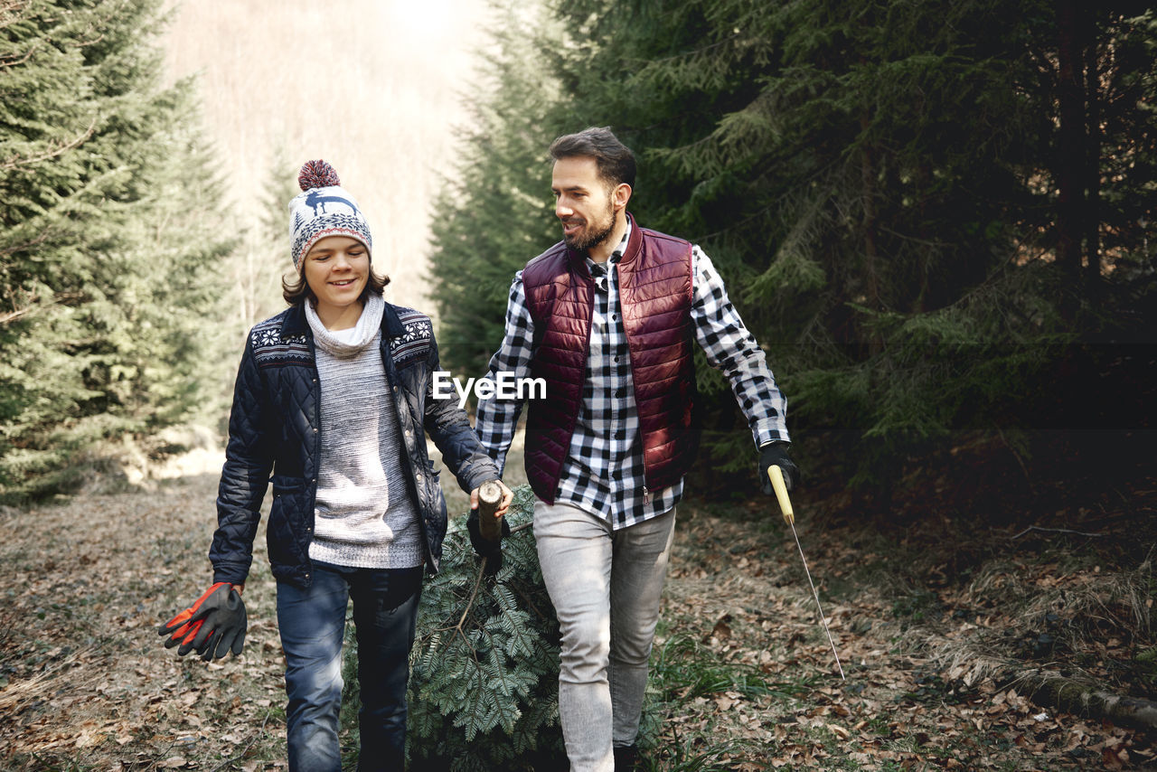 Happy father and son walking with branch in forest