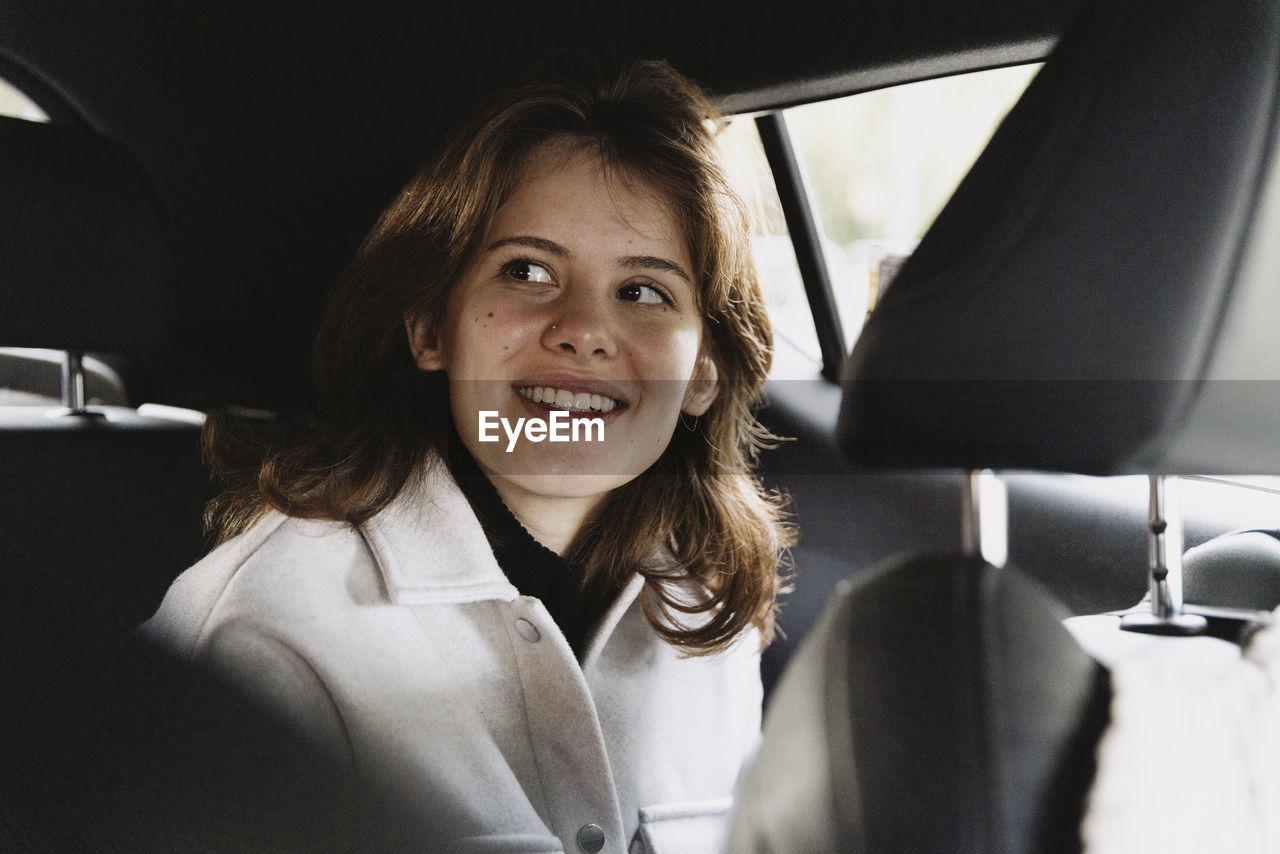 Smiling woman day dreaming while sitting in car on vacation