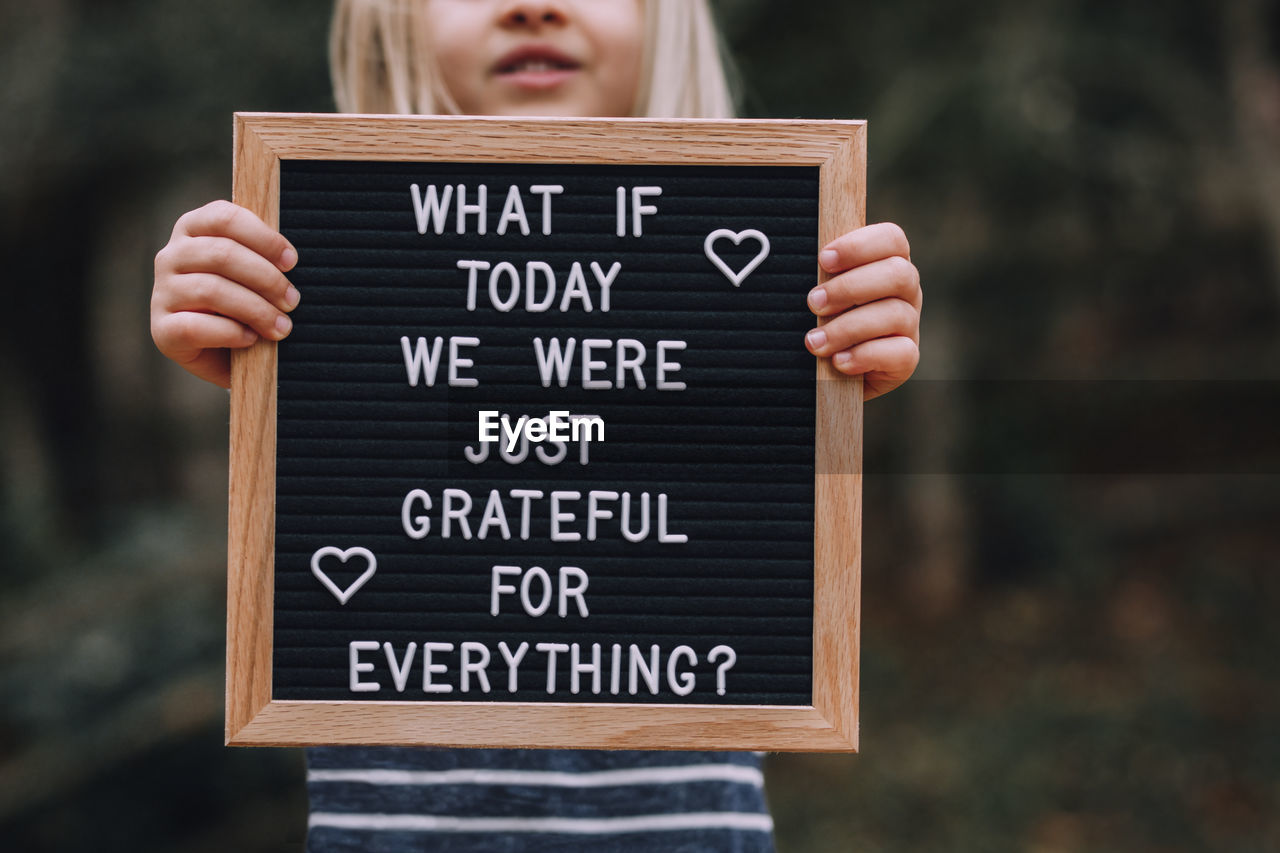 Midsection of girl holding text on blackboard