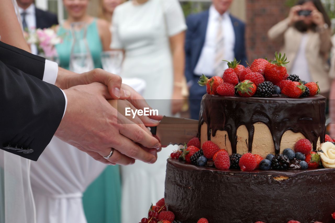 Cropped image of bride and groom cutting cake during wedding