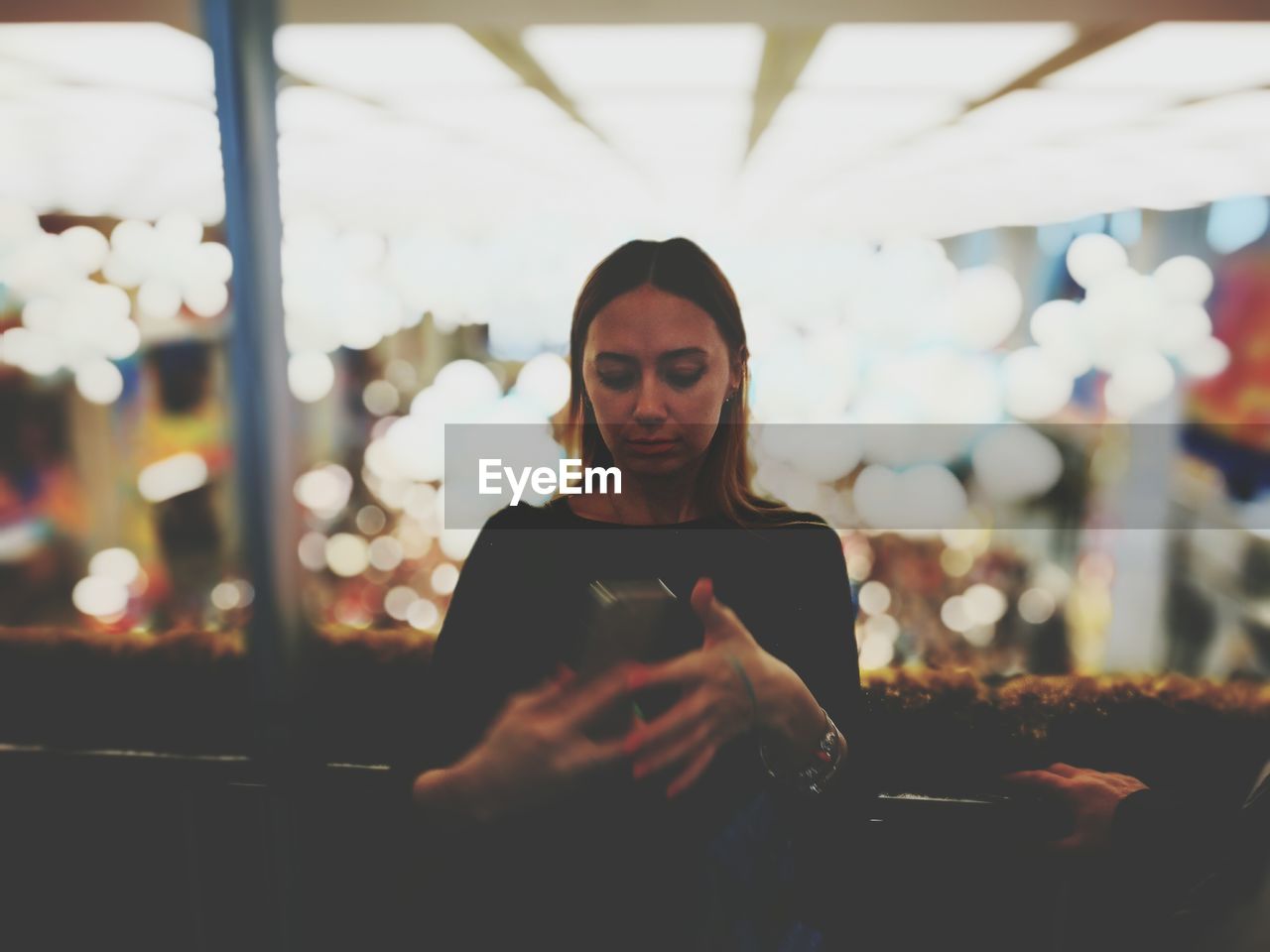 Young woman using mobile phone while standing against illuminated lights