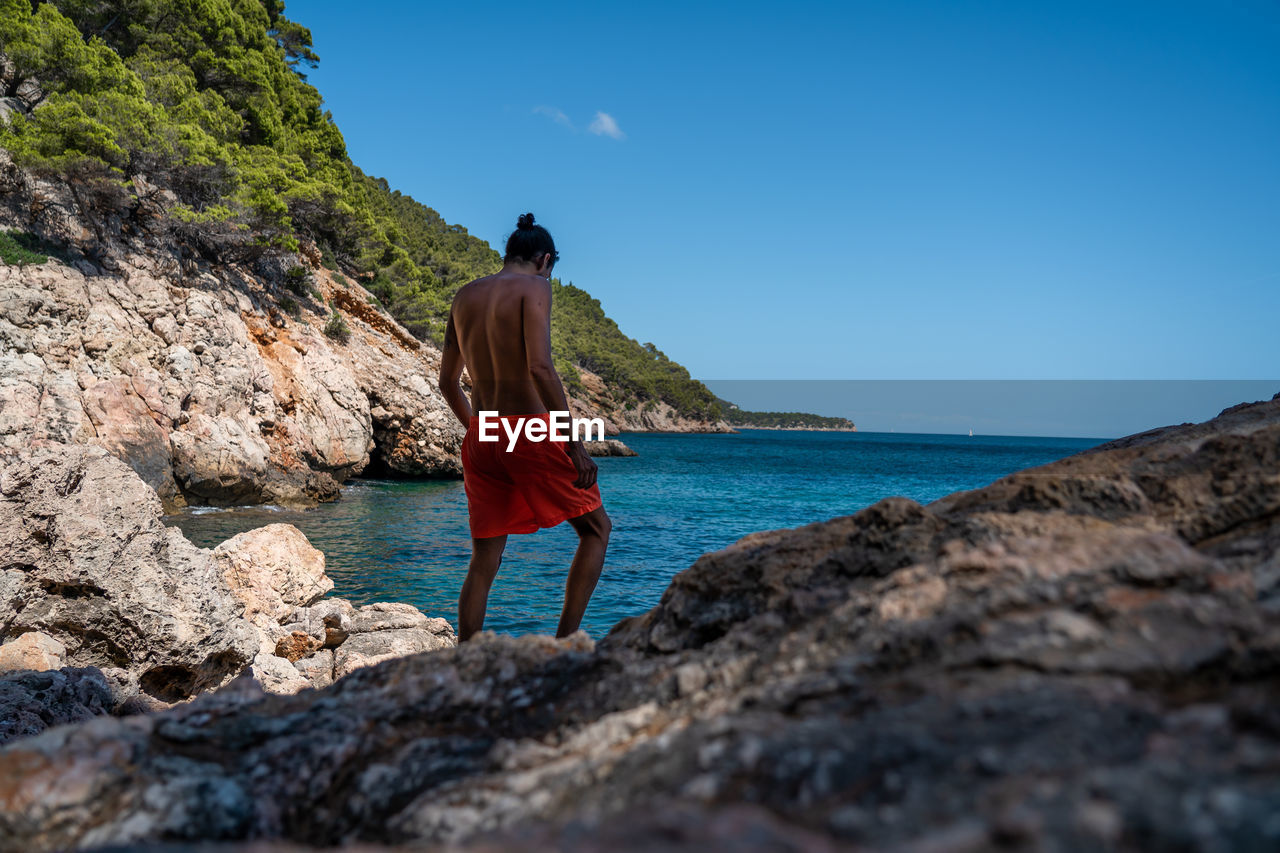 Rear view of man standing on rock by sea against sky