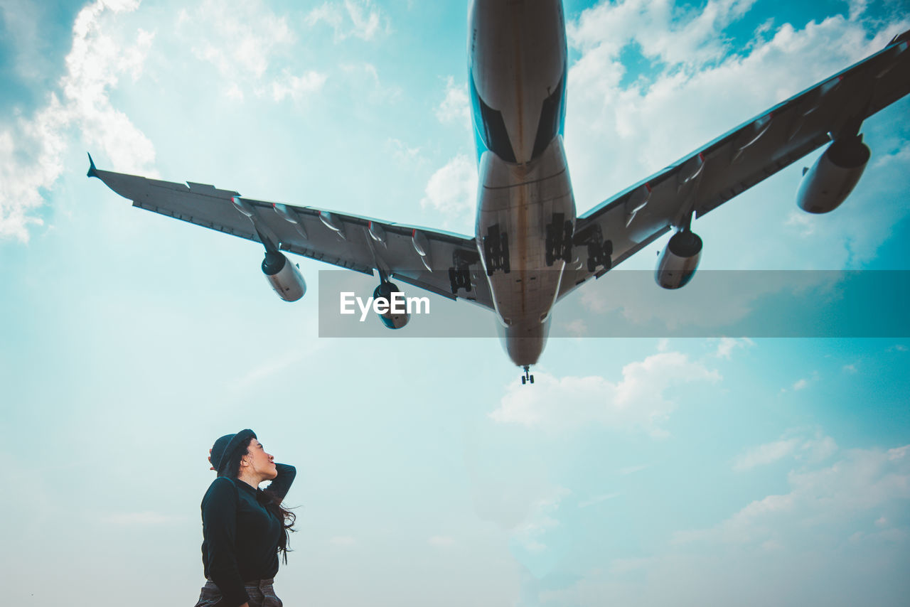 Woman looking at airplane flying against sky