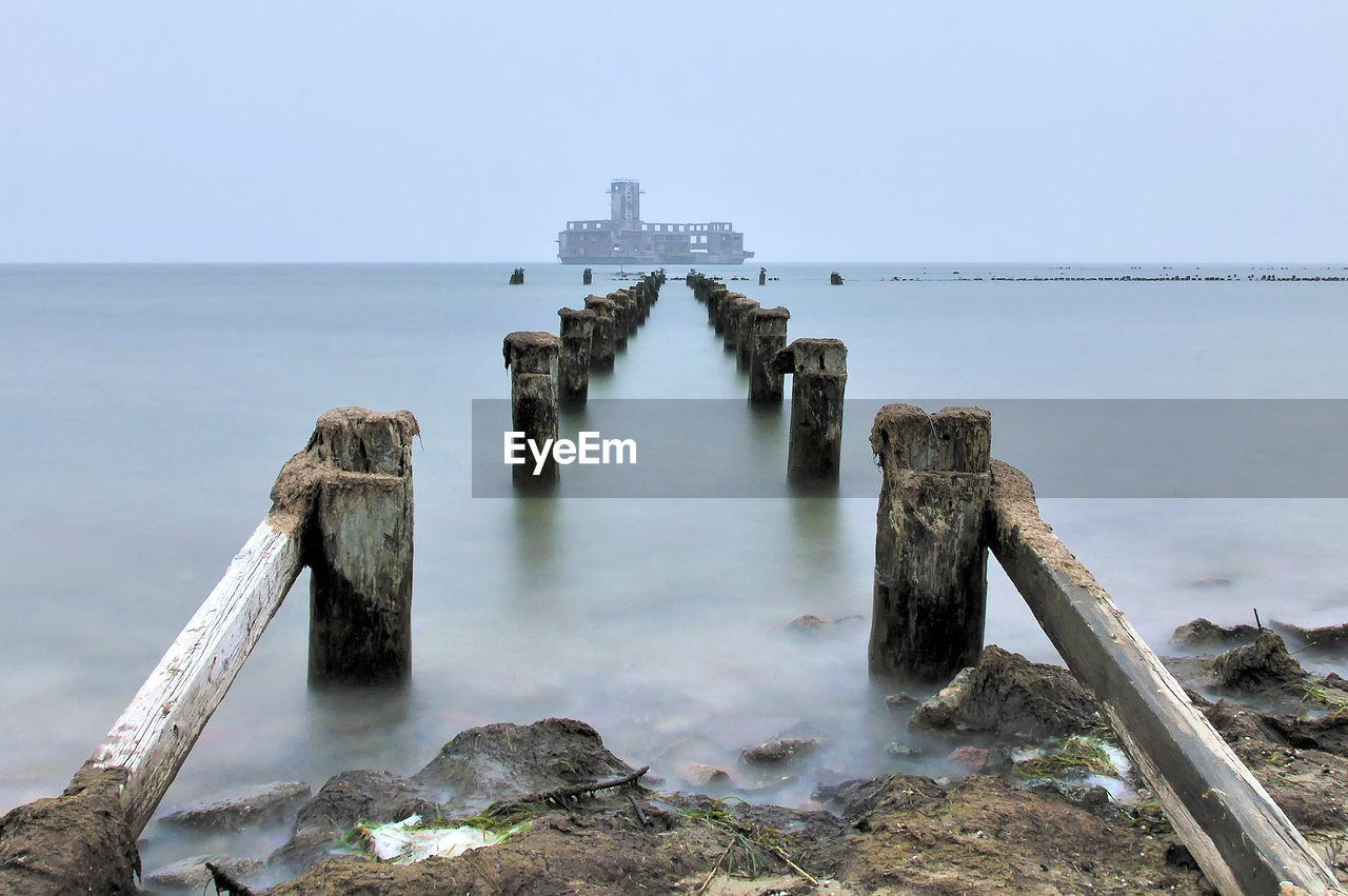 WOODEN POSTS ON SEA AGAINST SKY