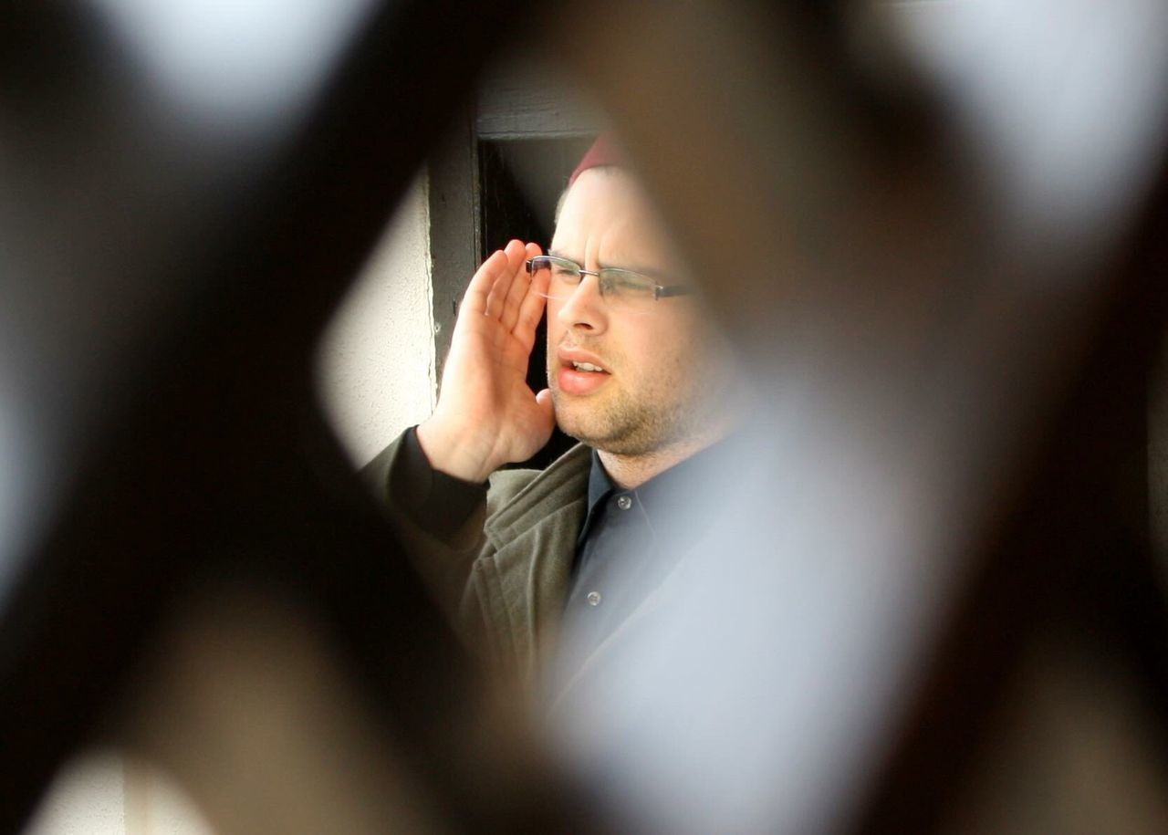 Muslim man calling for prayer in mosque seen through fence