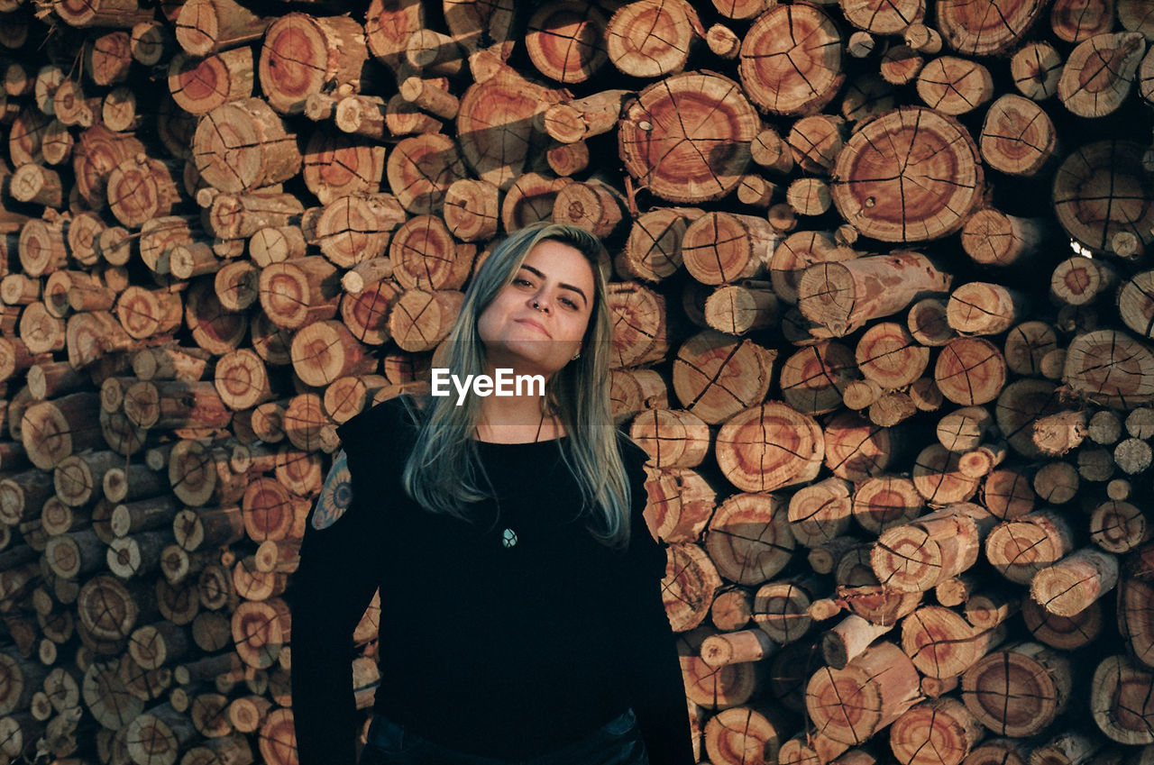 Portrait of woman standing against stacked logs