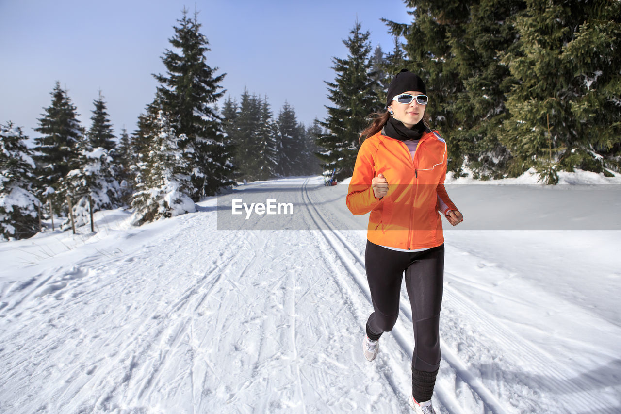 Woman running on snow covered field against sky