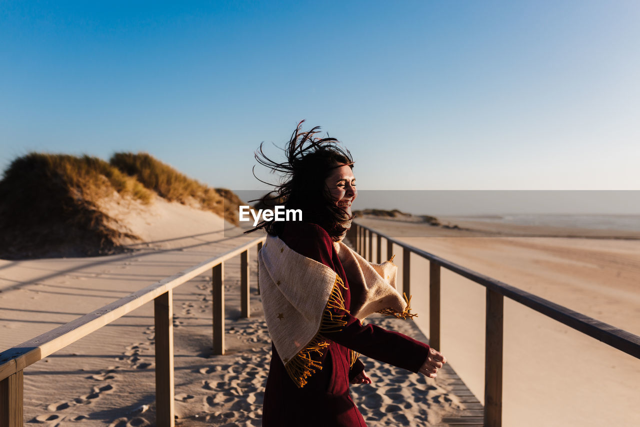 Woman looking away while standing by railing against clear sky