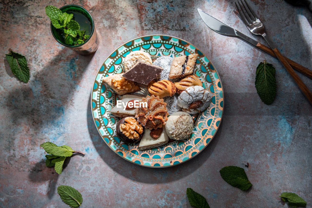 From above of baklava and biscuits with moroccan peppermint tea near knife and fork placed on table decorated with mint leaves