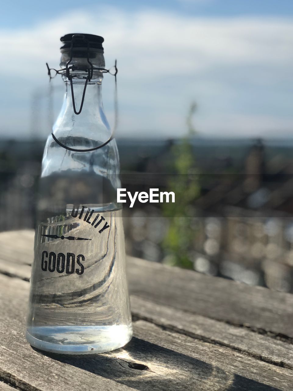 CLOSE-UP OF GLASS BOTTLE WITH JAR ON TABLE AGAINST SKY