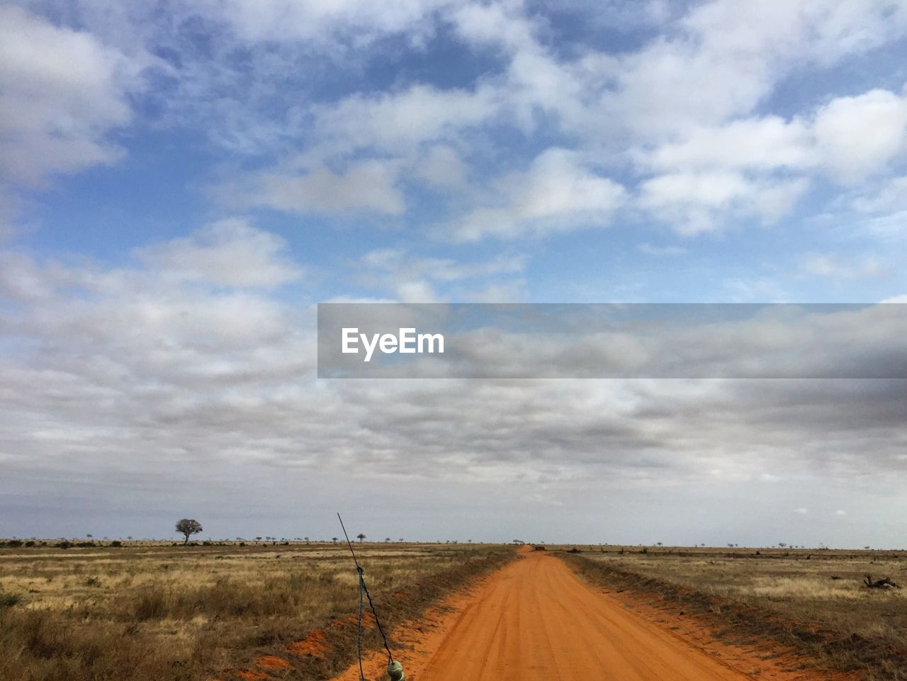 DIRT ROAD PASSING THROUGH FIELD AGAINST CLOUDY SKY