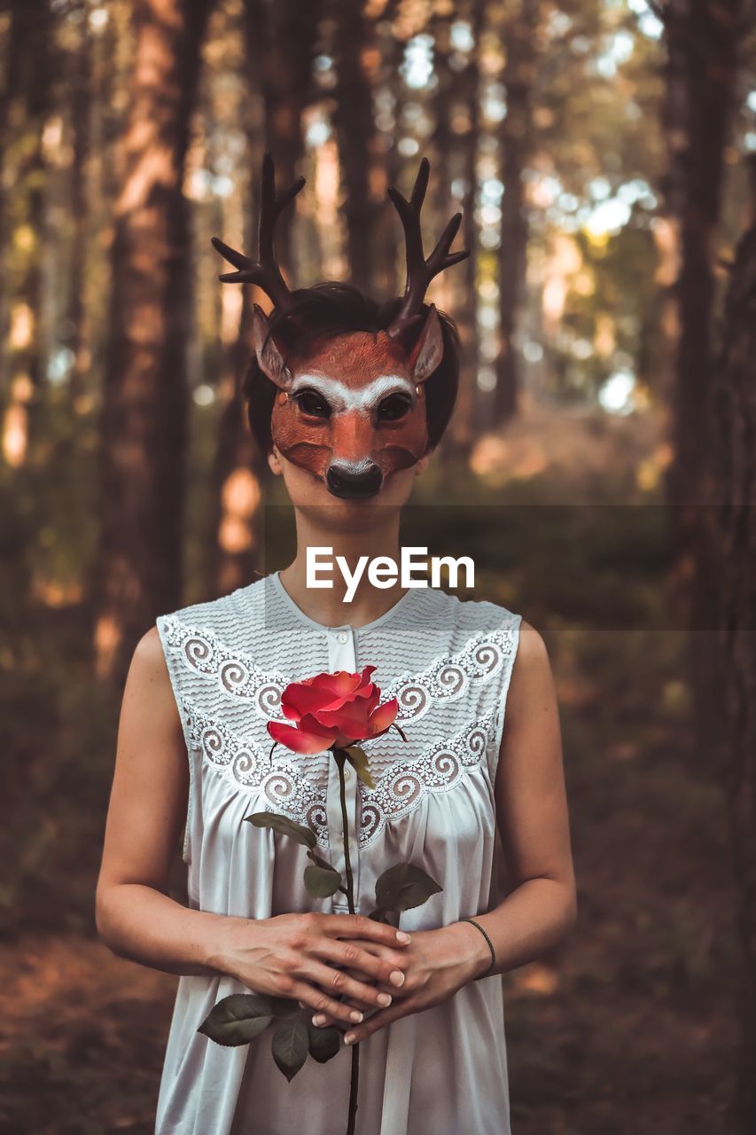 Close-up of woman holding rose while wearing mask in forest