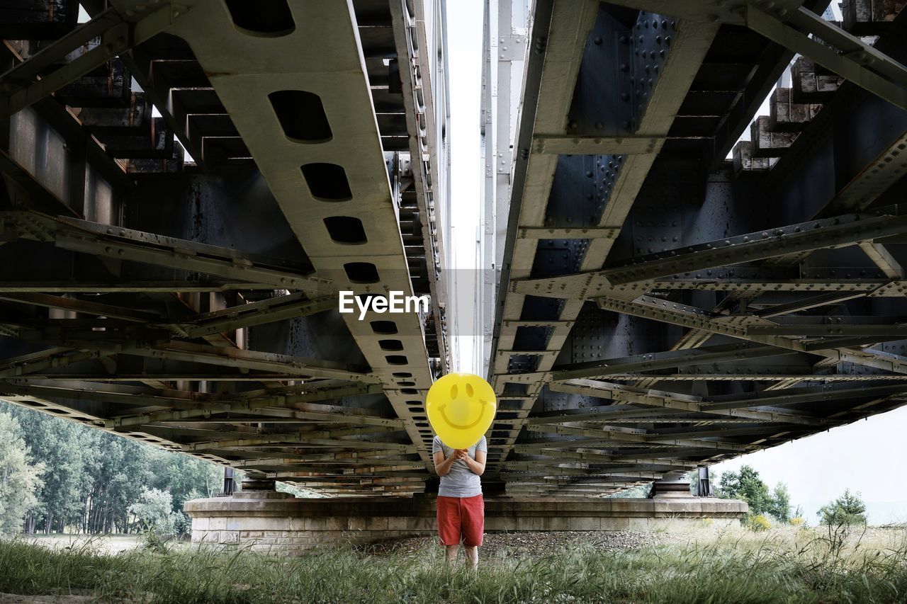 Man holding balloon while standing under bridge