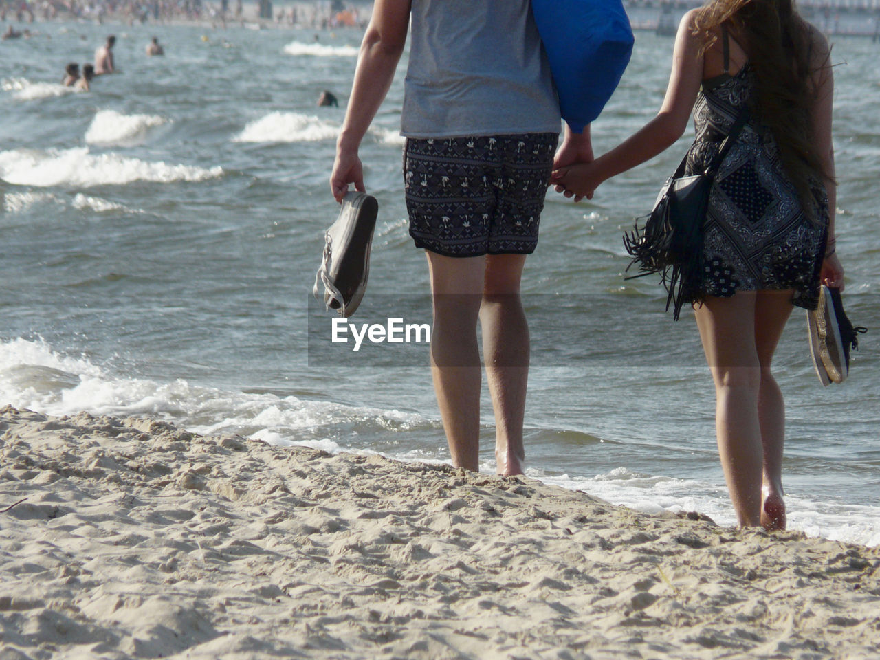 Rear view of couple holding hands and walking shore of beach