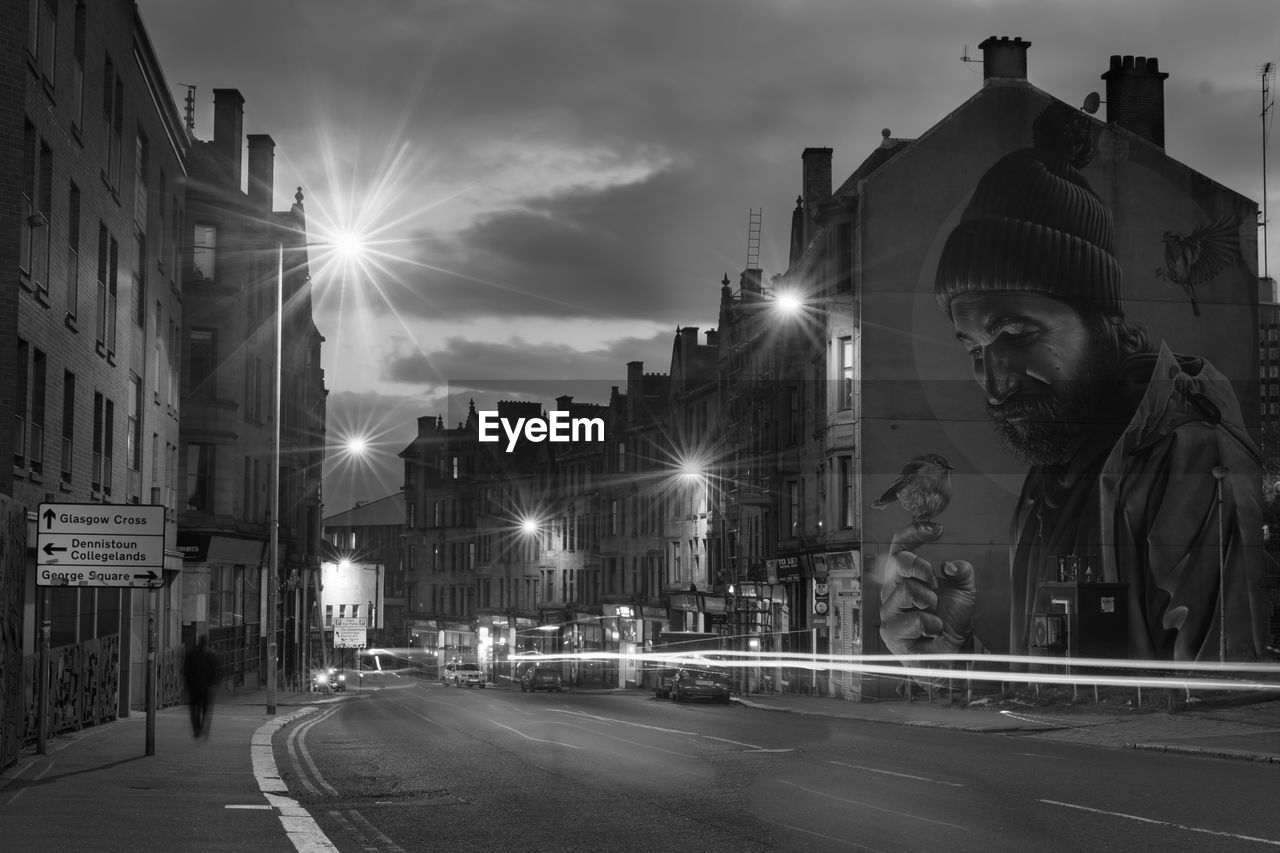 STREET AMIDST BUILDINGS AGAINST SKY AT NIGHT