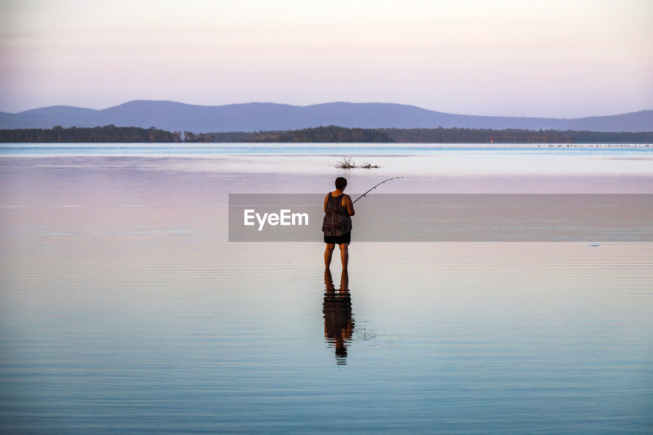 Rear view of woman fishing in lake during sunset