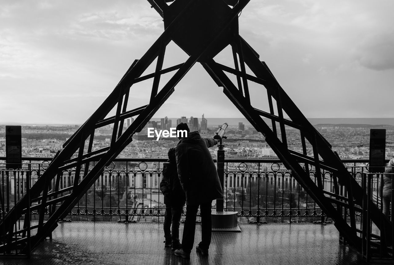 Man and child standing in eiffel tower against sky in city