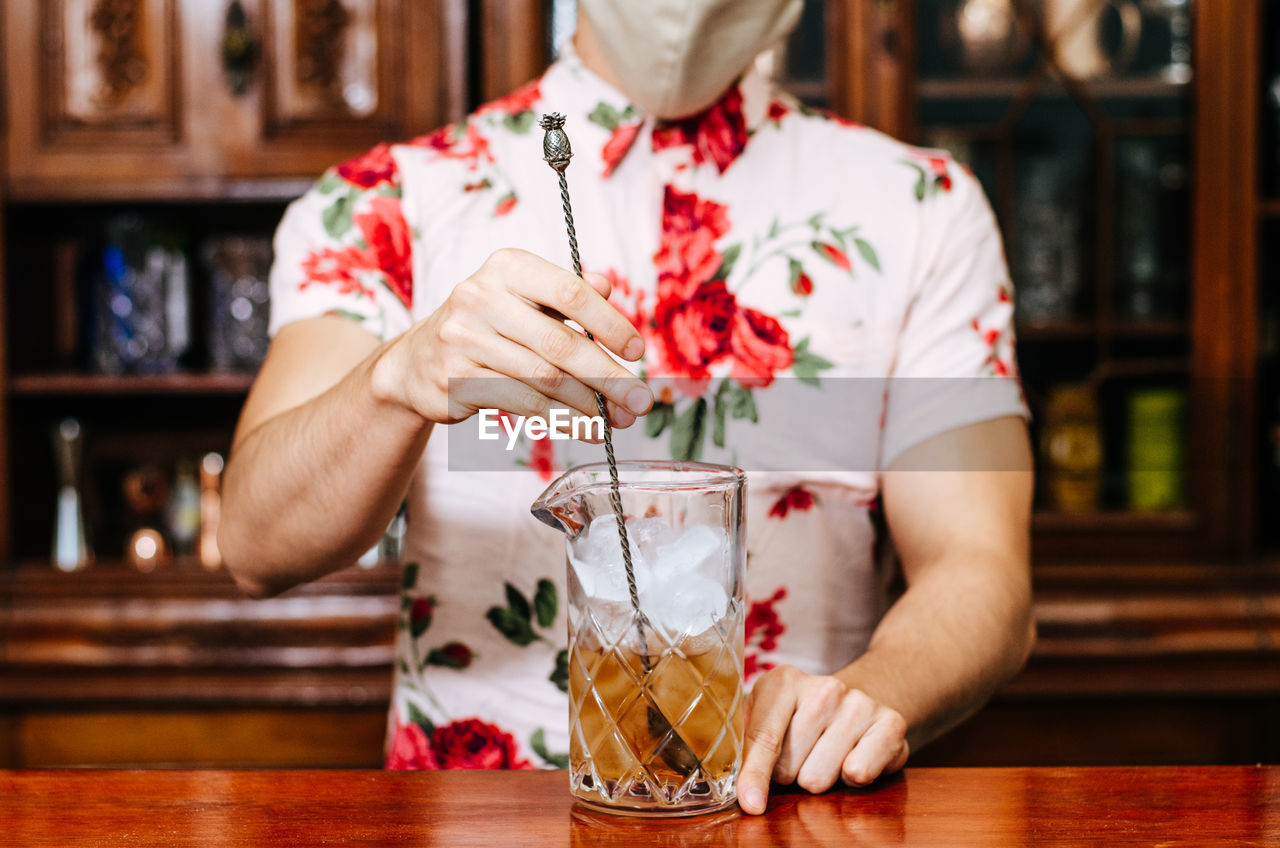 MIDSECTION OF MAN HOLDING ICE CREAM WITH GLASS ON TABLE