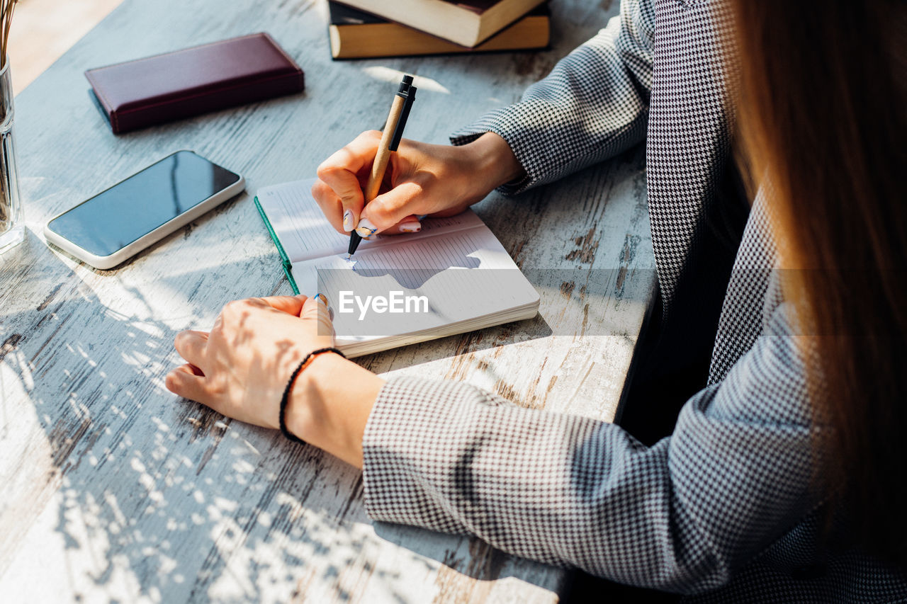 A young woman is sitting at a table writing in a notebook. a business woman works as a freelancer .