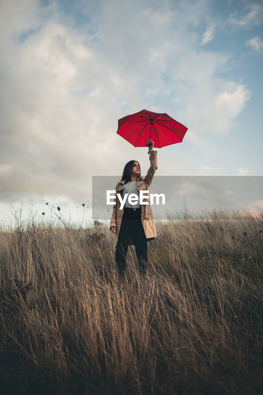 WOMAN STANDING ON FIELD AGAINST SKY AT DUSK