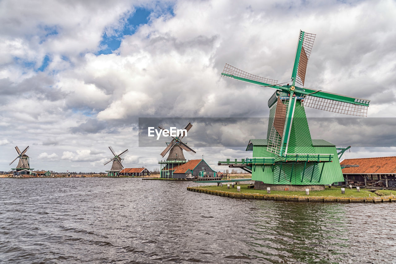 Traditional windmills by river against cloudy sky at zaanse schans