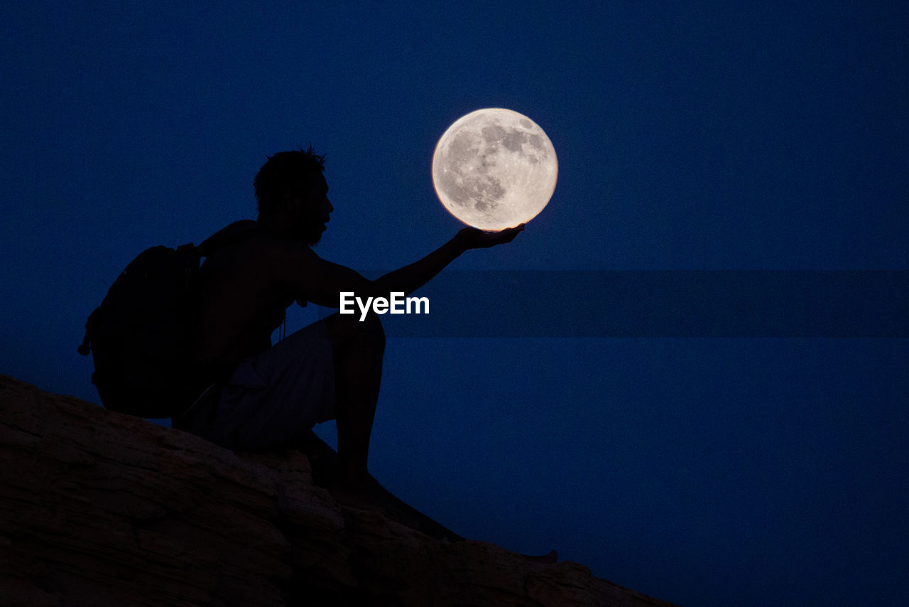 Optical illusion of man holding full moon in clear blue sky