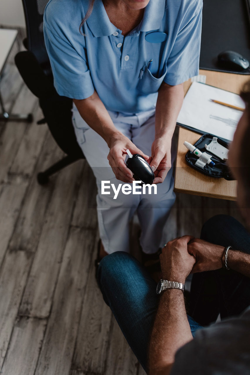 High angle view of nurse holding glaucometer while sitting with male patient in hospital