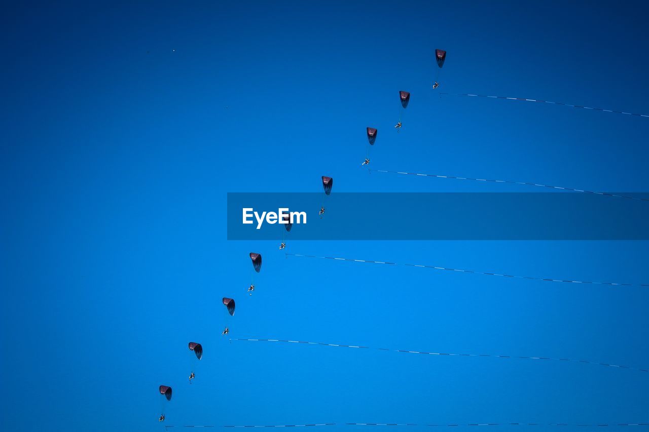 Low angle view of people paragliding against clear blue sky during sunny day